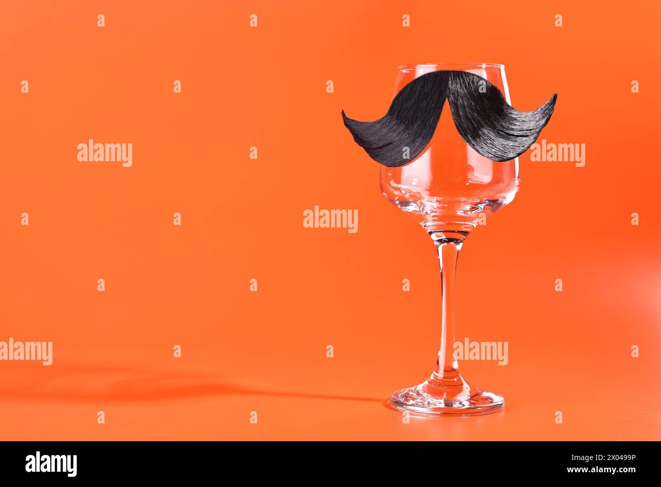 Man's face made of artificial mustache and wine glass on orange background. Space for text Stock Photo