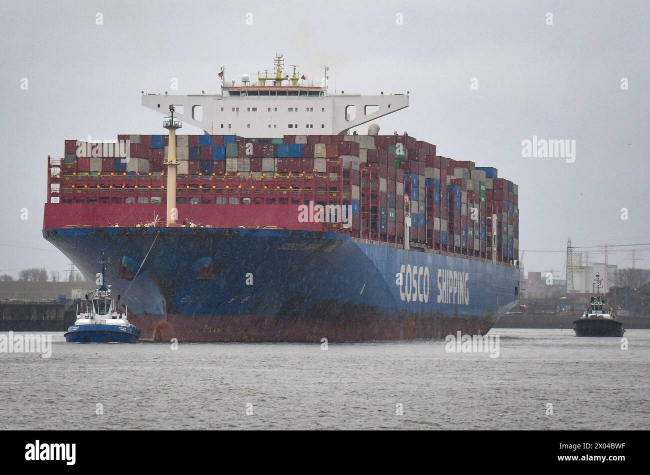 Bugsiert von zwei Schleppern faehrt ein Containerschiff bei widrigem Wetter aus dem Containerhafen in Hamburg hinaus auf die Elbe. Jaehrlich laufen rund 13.000 Seeschiffe den Hamburger Hafen an, den zweitgroessten Europas. Foto: Rothermel *** Towed by two tugs, a container ship sails out of the container port in Hamburg onto the Elbe in bad weather Every year, around 13,000 ocean-going vessels call at the port of Hamburg, the second largest in Europe Photo Rothermel Stock Photo