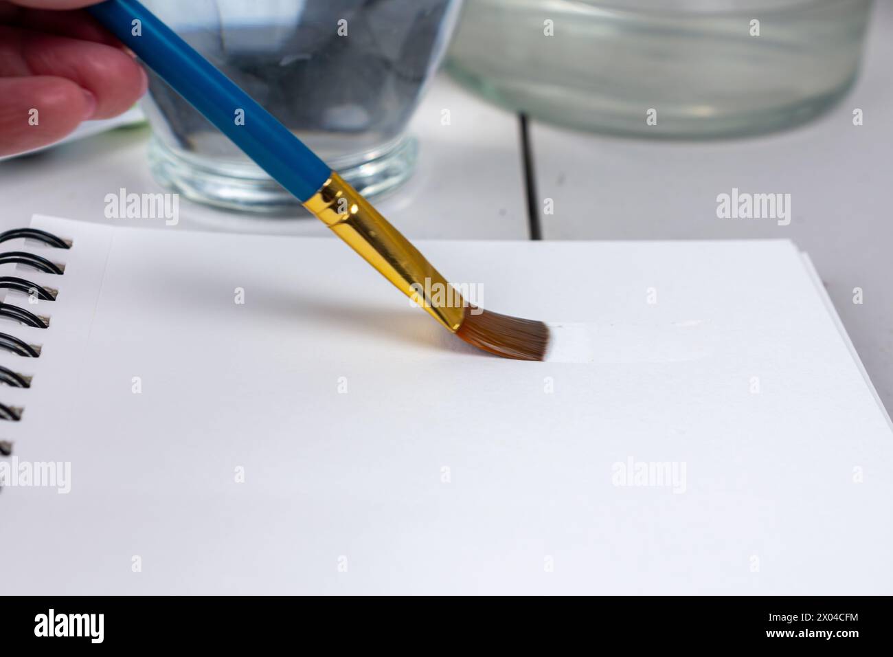 An artist applies water to watercolor paper with a large flat brush. Stock Photo