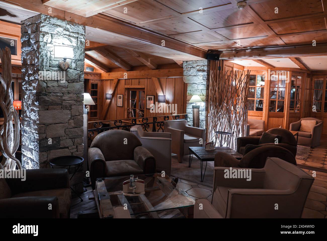 Rustic lodge lounge with wooden beams, stone tiles, cozy seating, and