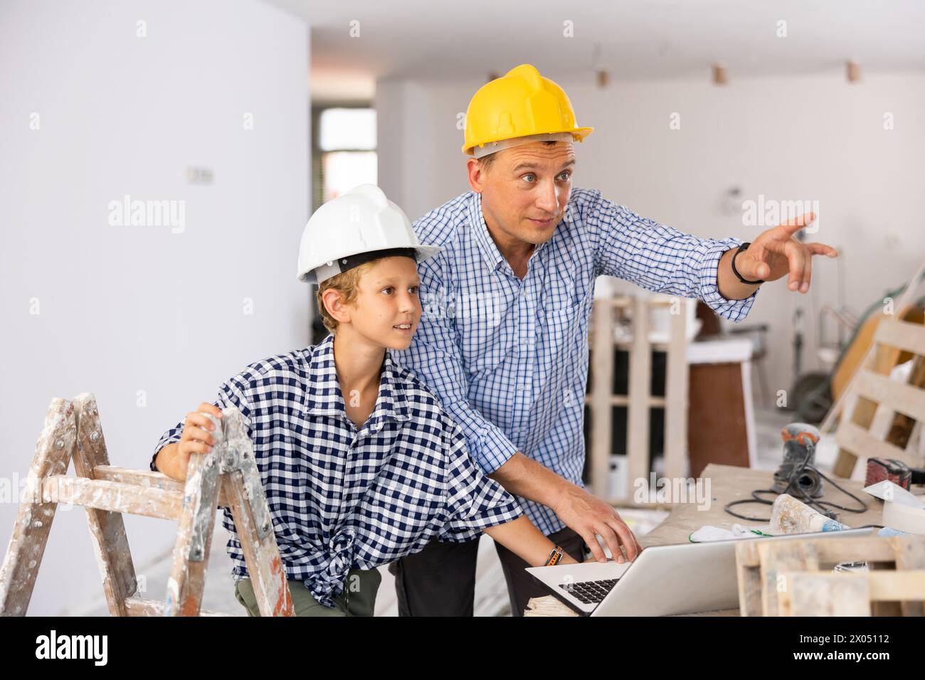Man architect and boy using laptop while discussing working process in house being renovated Stock Photo