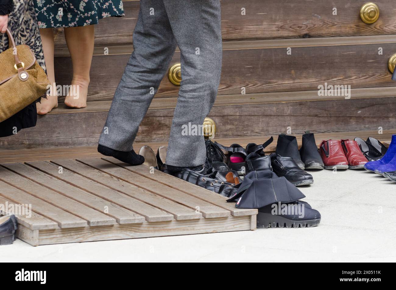 A row of shoes are lined up on a wooden platform. The shoes are of various colors and styles, including black, brown, and white. Concept of organizati Stock Photo