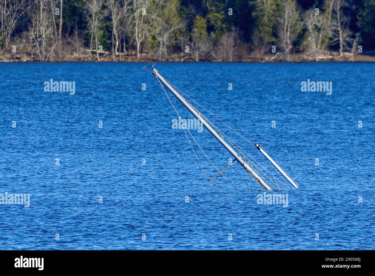 The masts of a sunken sailboat sticking up at an angle from blue water. Stock Photo