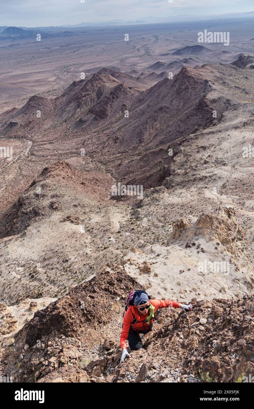 woman scrambling up a desert mountain in the Turtle Mountains of eastern California Stock Photo