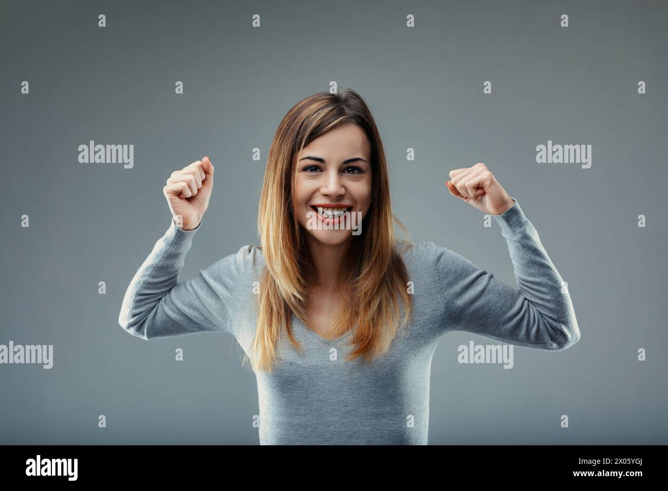 Gleeful expression paired with a victor's pose defines the lady's exultant state in grey Stock Photo
