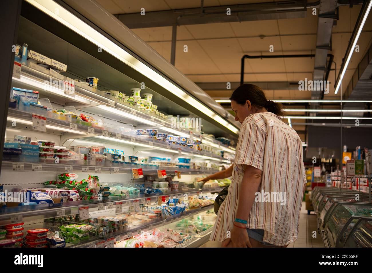 Ancona, Italy - 16 Sep 2023: A young girl in a short-sleeved shirt chooses groceries in an Italian supermarket. A beautiful young woman buys groceries Stock Photo