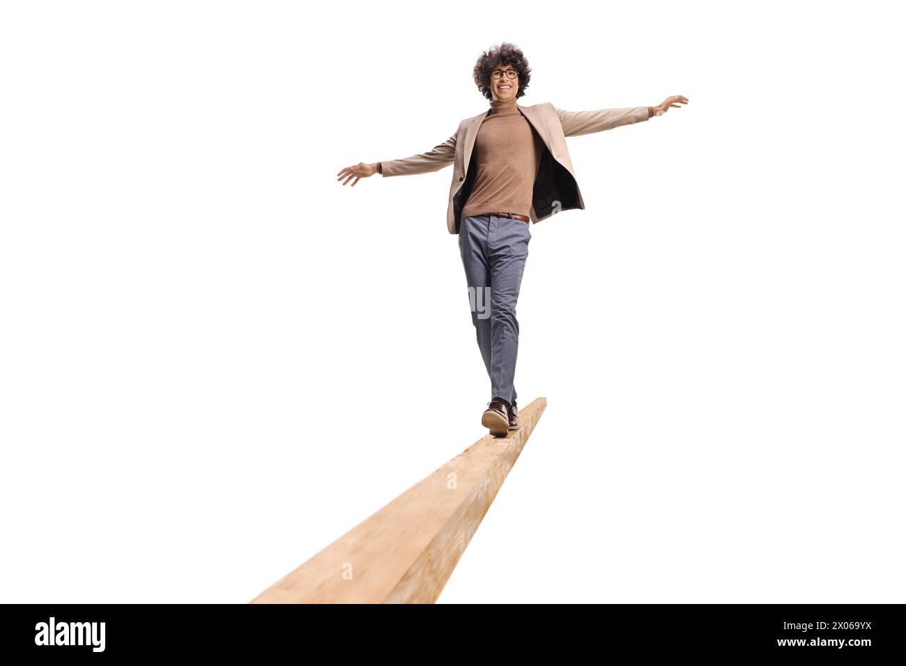 Young man with curly hair walking on a wooden beam and smiling isolated on white background Stock Photo