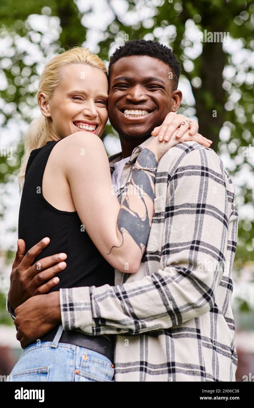 A happy, multicultural couple, a Black man and a Caucasian woman, embrace lovingly in a park setting. Stock Photo
