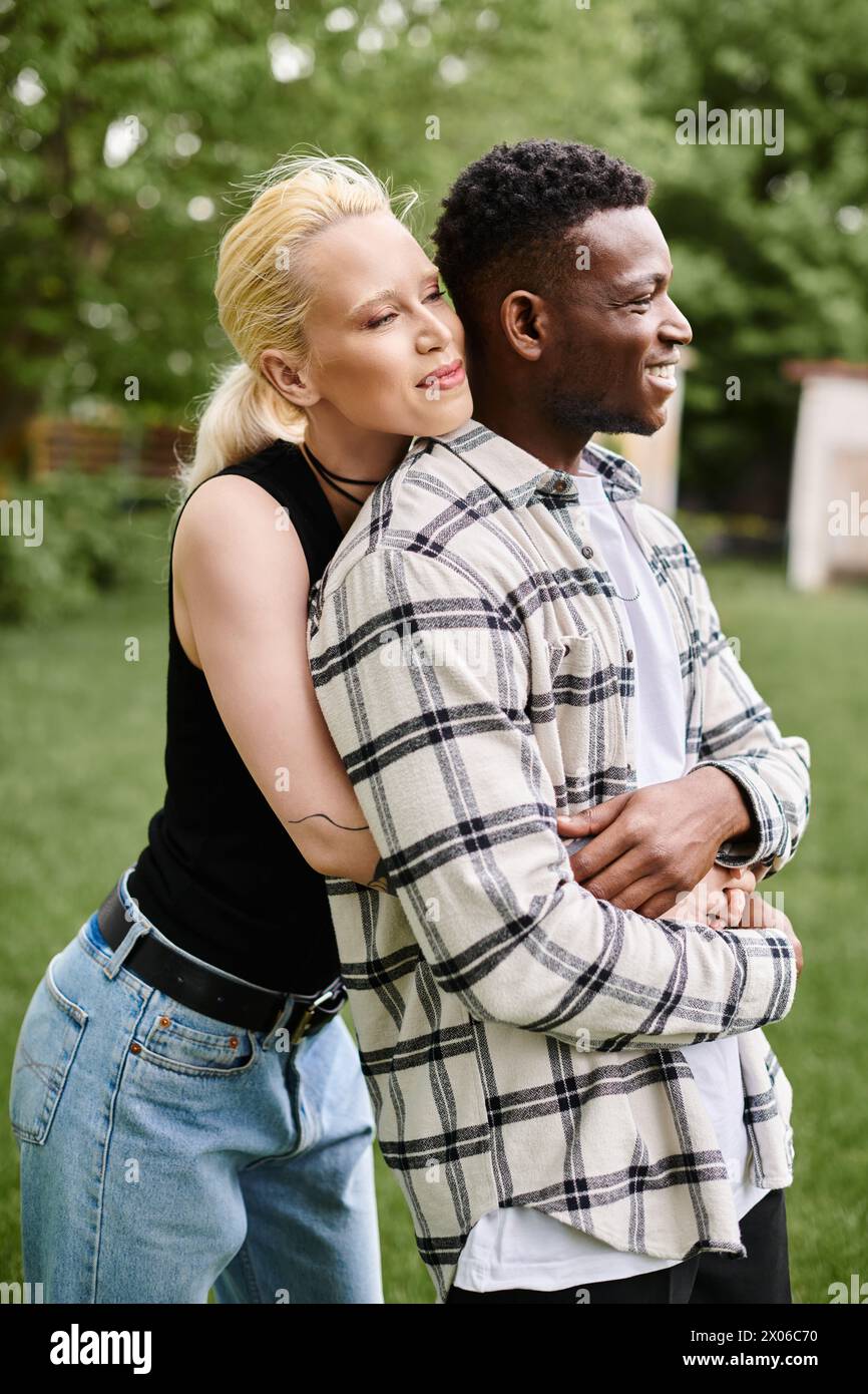 A multicultural couple, an African American man and a Caucasian woman, share a warm embrace amidst lush greenery in the park. Stock Photo