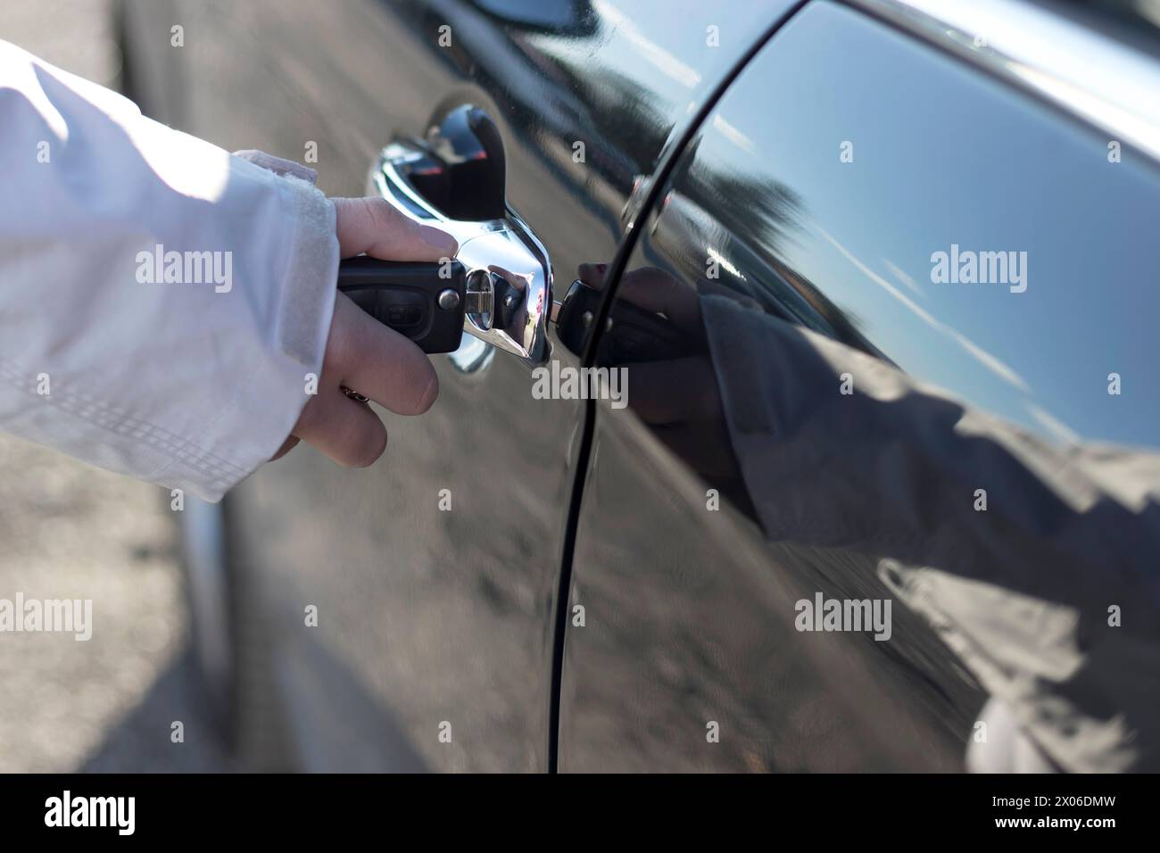Close-up of a hand holding car keys and key fob, about to unlock a shiny car door. Focus on security and access Stock Photo