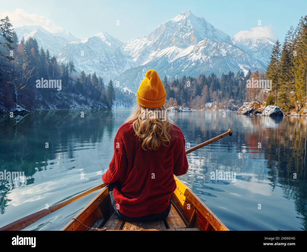 Blonde white woman on a boat paddling on lake with mountains and winter forest Stock Photo