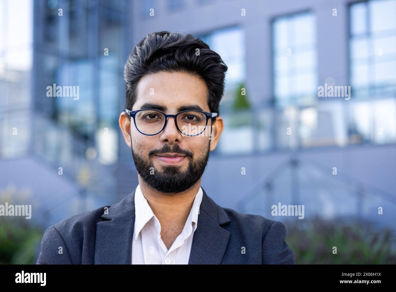 Close-up portrait of a young Indian man in a suit and glasses standing ...