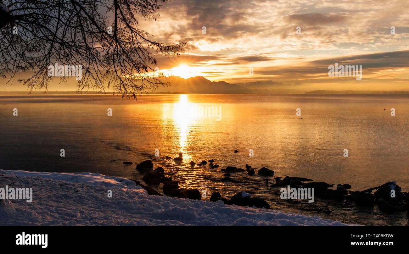golden light of the setting winter sun over the Alpine panorama reflected in the lake, Germany, Bavaria, Lake Chiemsee Stock Photo