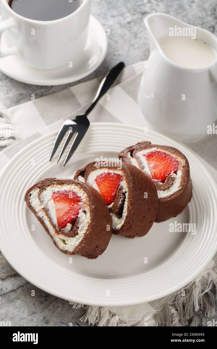 Sweet chocolate cake roll filled with strawberries and cream cheese served with coffee close-up on the table. Vertical Stock Photo
