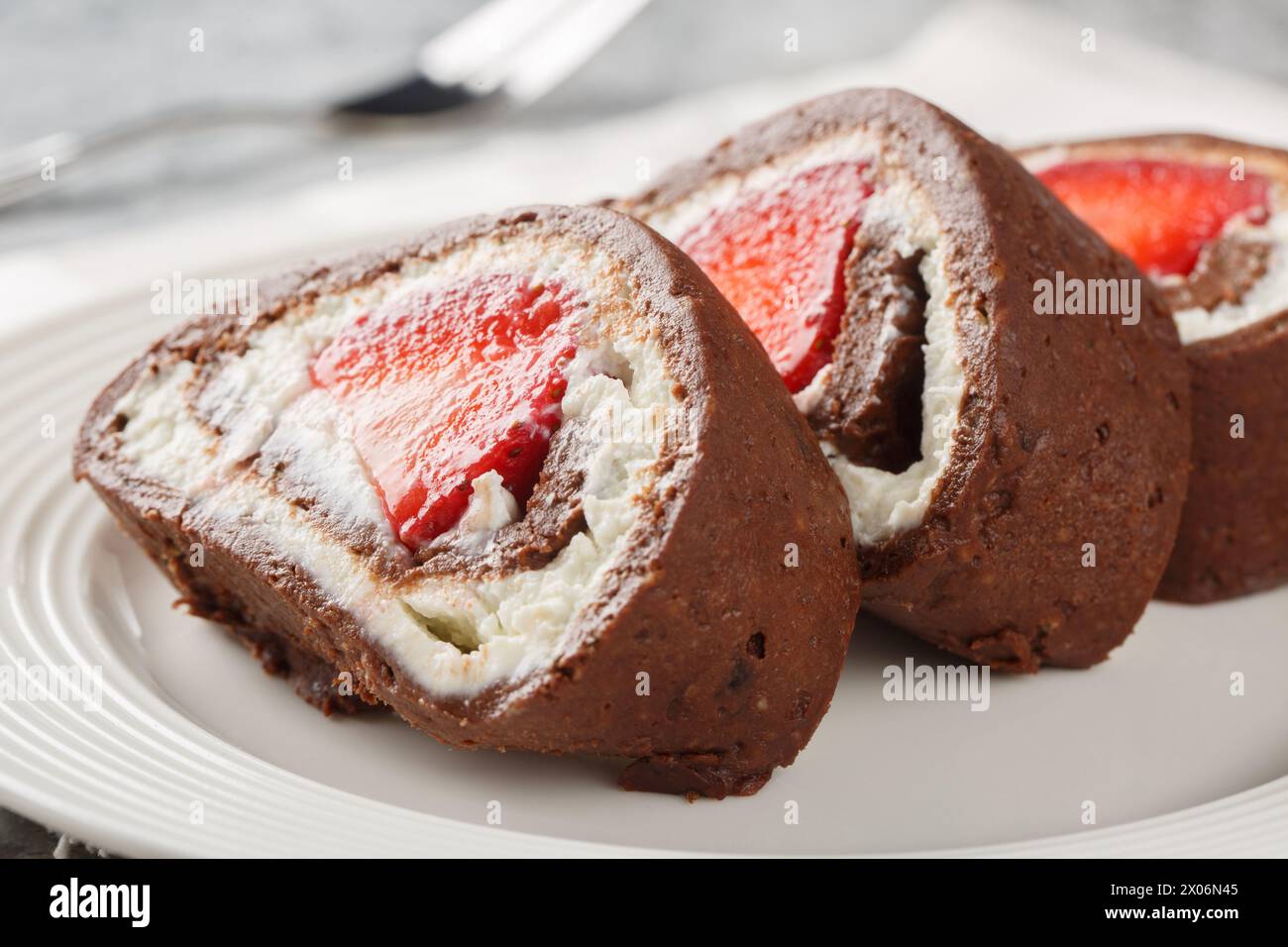 Pieces of chocolate cake roll with strawberries and cream cheese close-up on a plate. Horizontal Stock Photo