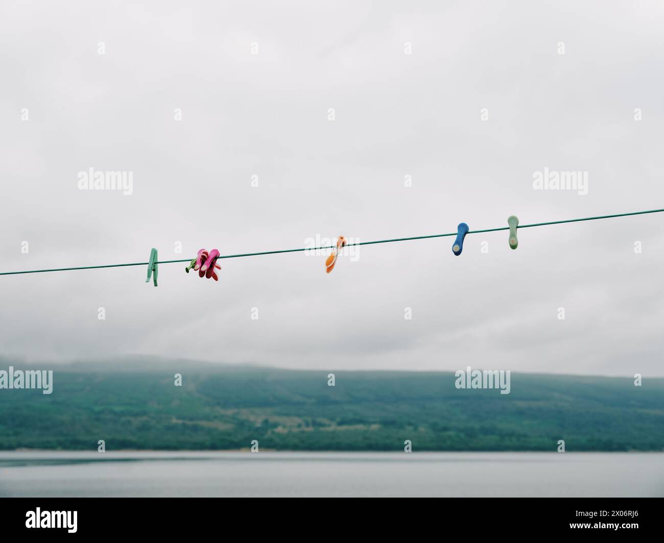 A green washing line with coloured plastic clothes pegs empty with a grey sky and sea background - clothes line, washing line, laundry line Stock Photo