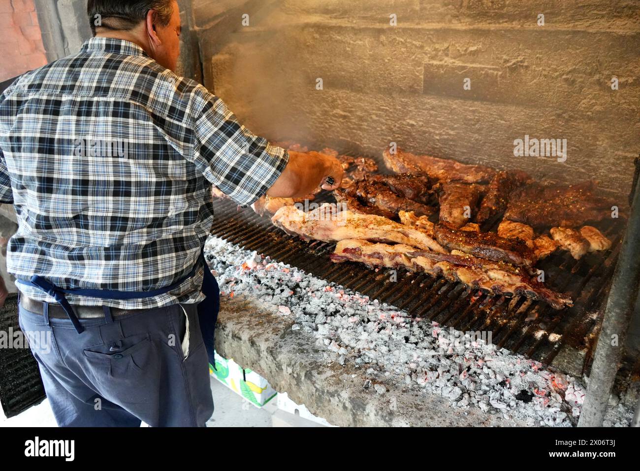 A man cooking over a bbq grill heated by hot coals. Stock Photo