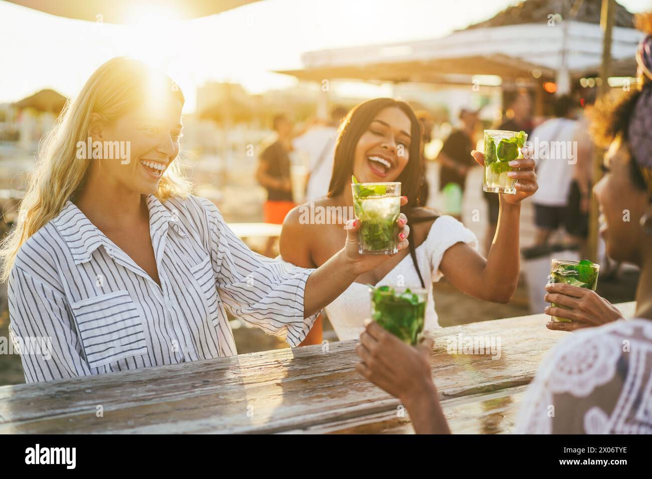 Happy girls cheering with mojitos on the beach at chiringuito sunset party - Summer vacation and people lifestyle concept - Main focus on left female Stock Photo