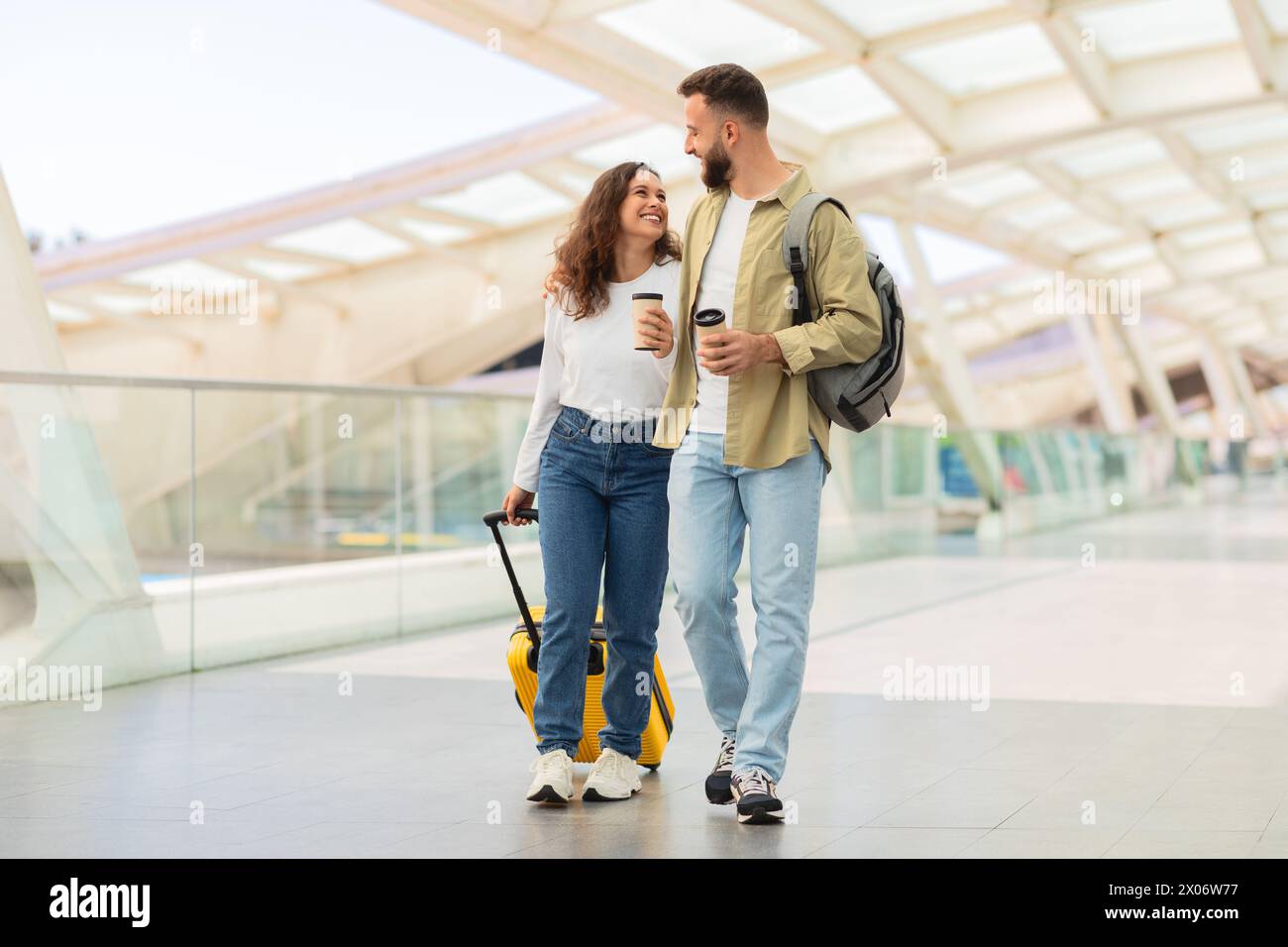 Man and Woman Walking Through Airport With Luggage And Takeaway Coffee Stock Photo