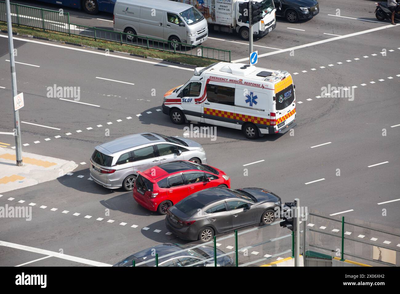 Elevated view of three cars stop after the dotted line to let the ambulance cross the junction first. Stock Photo