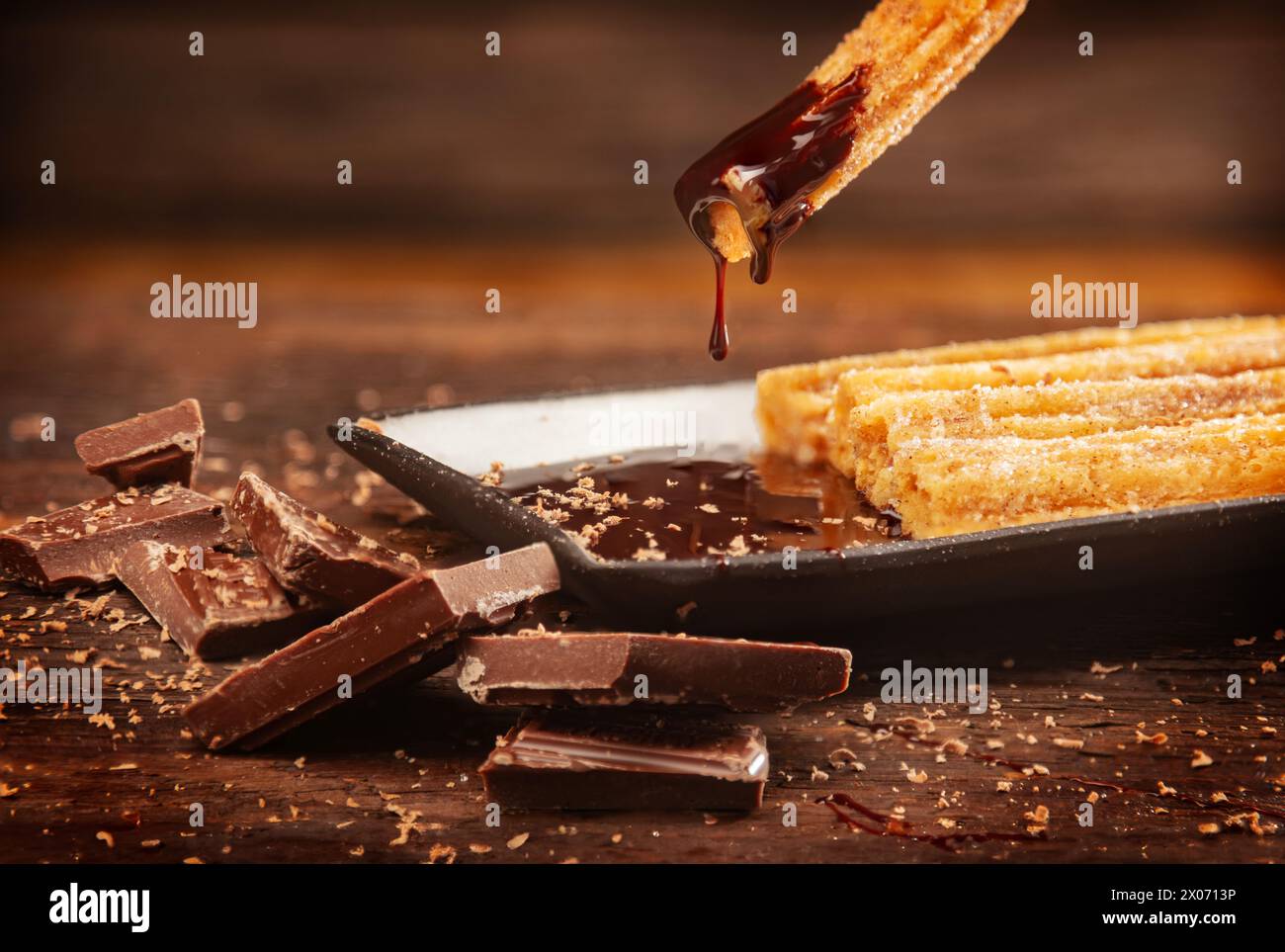 Five Fresh Churros with chocolate dipping sauce on wood background wand chocolate chunks on rustic plate Stock Photo