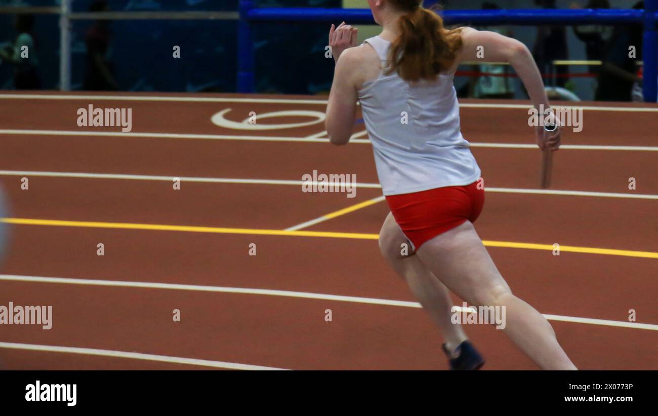 Female runner running fast on a banked indoor track holding a baton