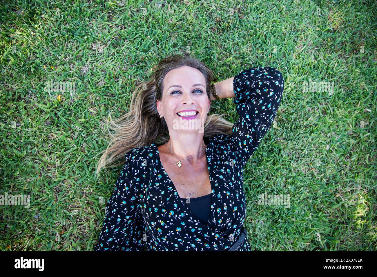 A woman is laying on the grass with smile on her face. Stock Photo