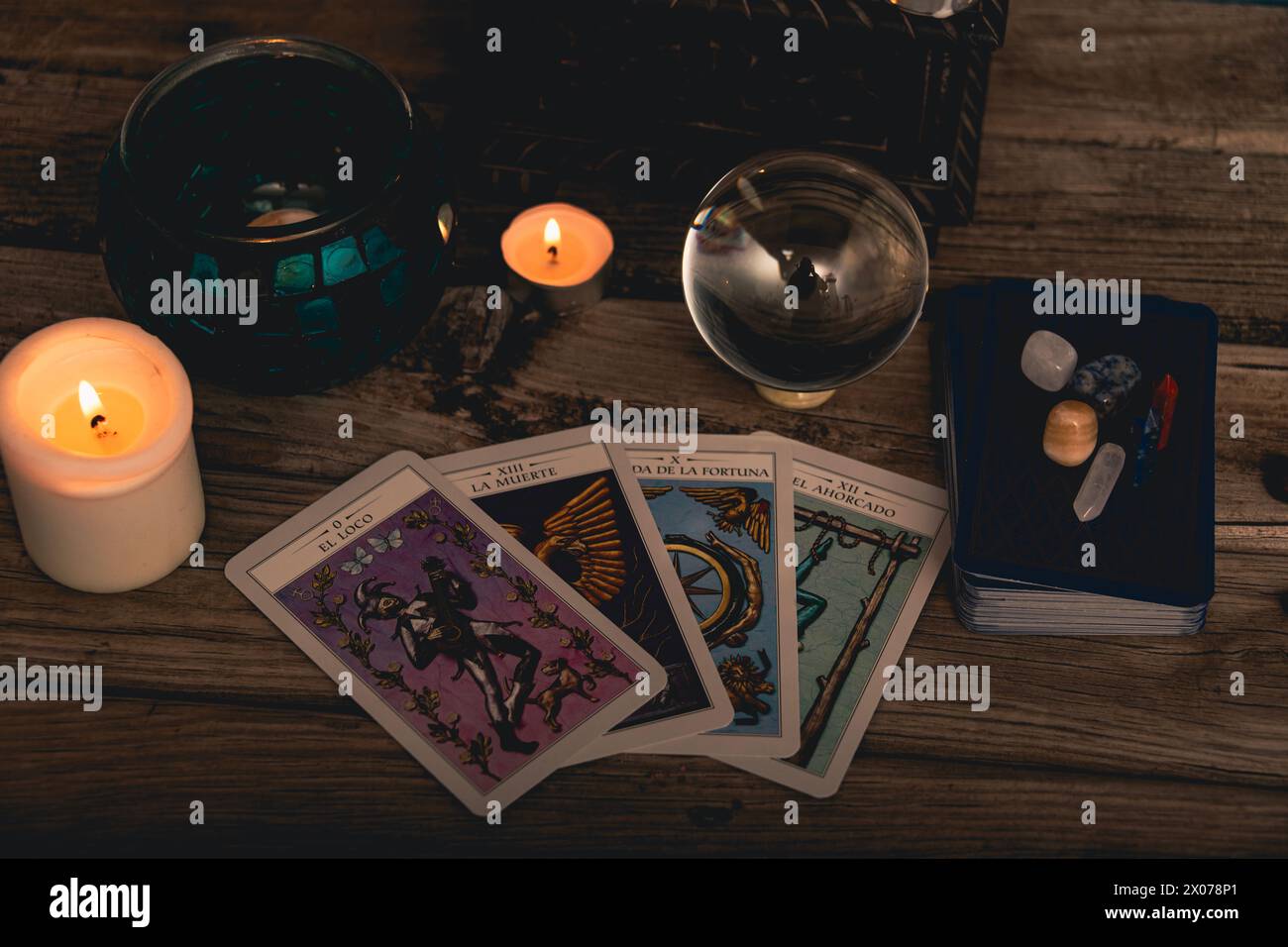 Tarot cards including The Fool and The Lovers alongside crystals and candles on a textured wooden table. Stock Photo