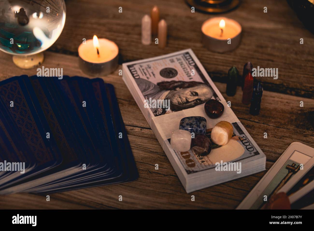 A tarot spread with The Fool card, hundred-dollar bills, and various crystals on a rustic wooden background with candles. Stock Photo