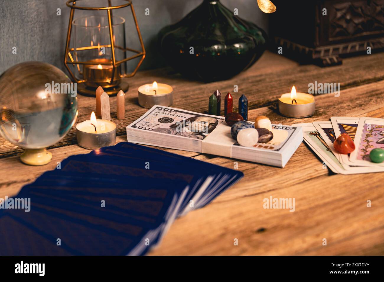 A tarot spread with The Fool card, hundred-dollar bills, and various crystals on a rustic wooden background with candles. Stock Photo