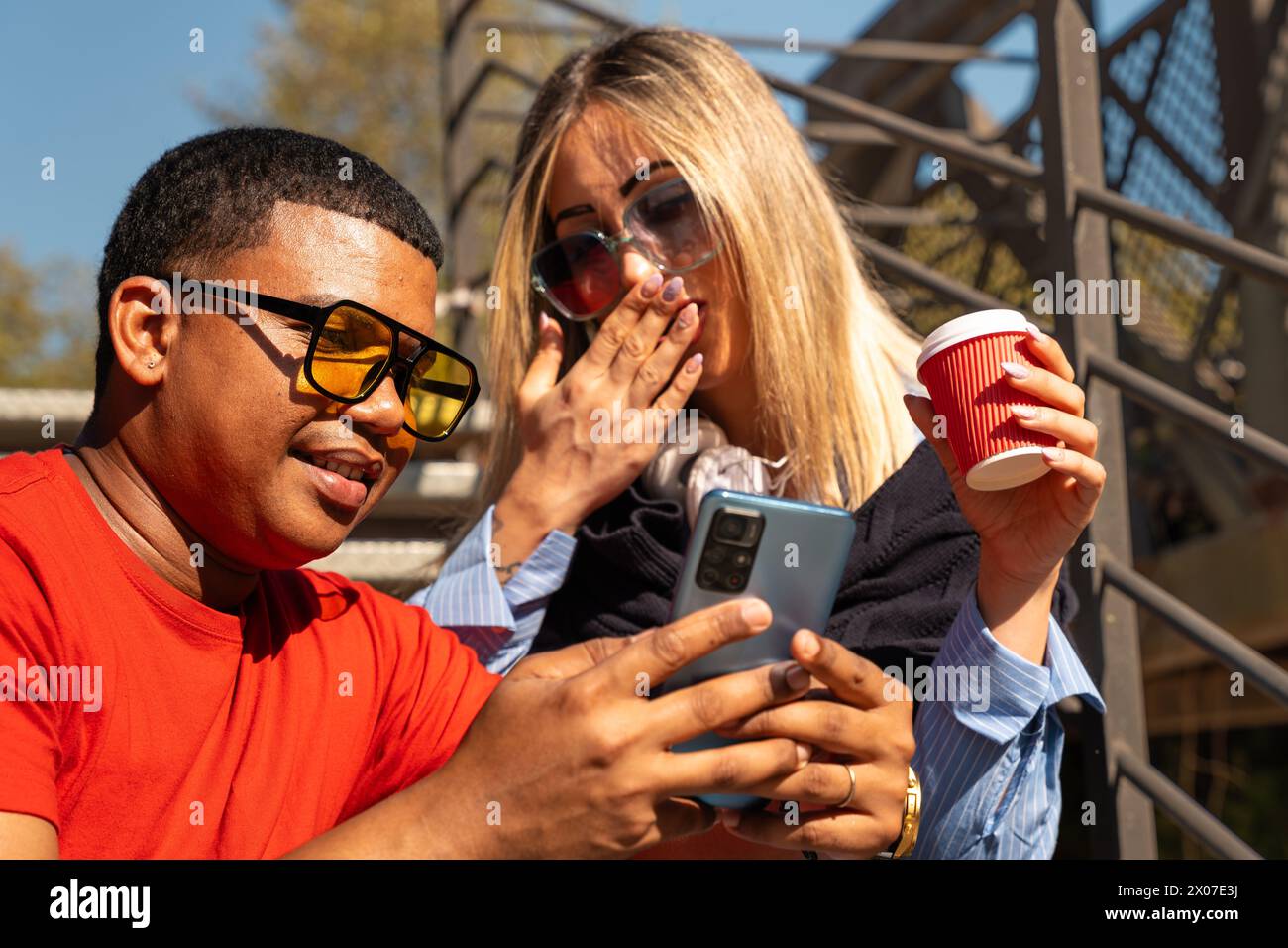 Happy interracial couple checking cell phone outdoors. Stock Photo