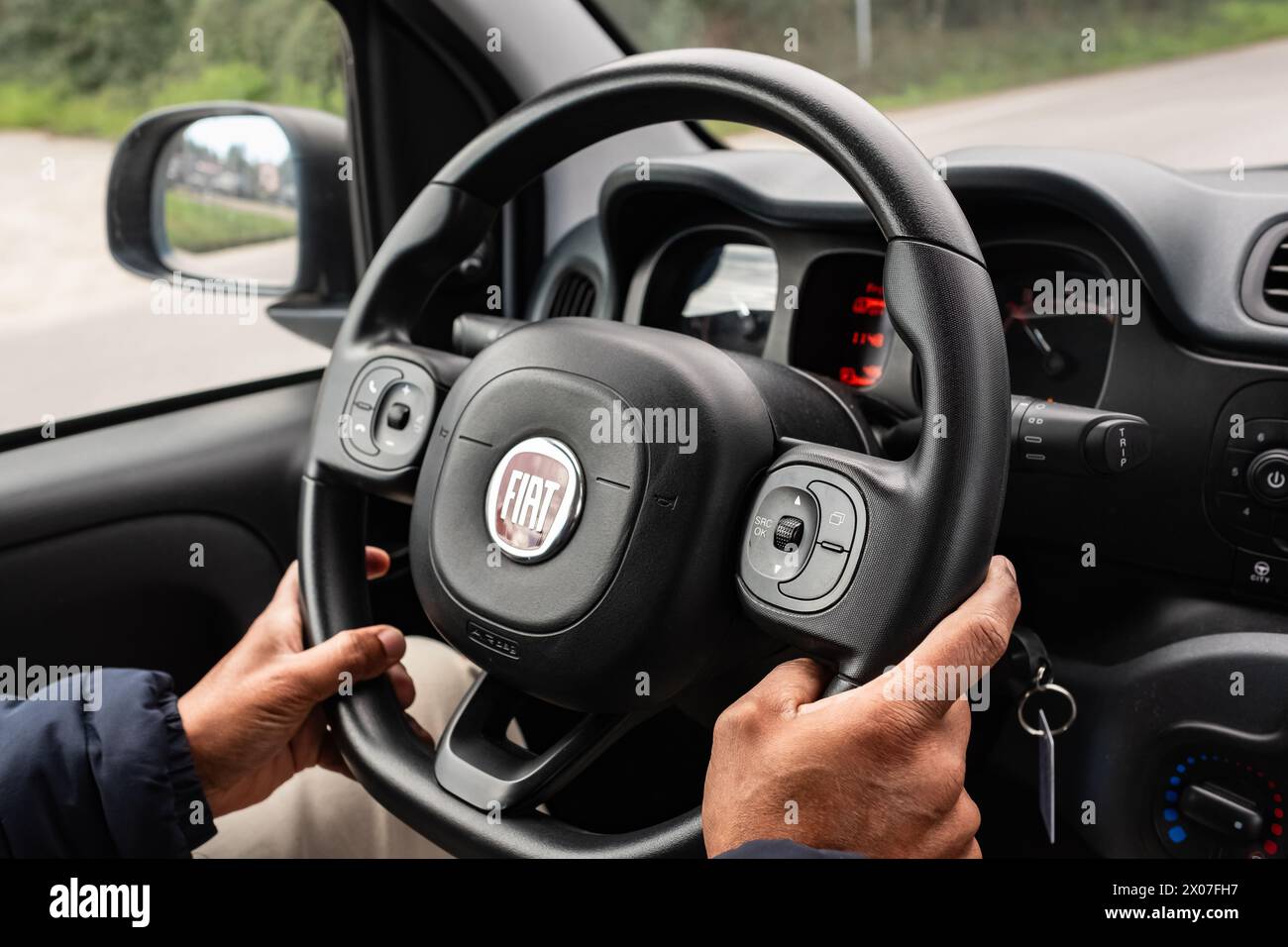 Interior of a car Fiat, steering wheel with a company logo. Hands on steering wheel of car driving on road. Man holds the steering wheel firmly with b Stock Photo