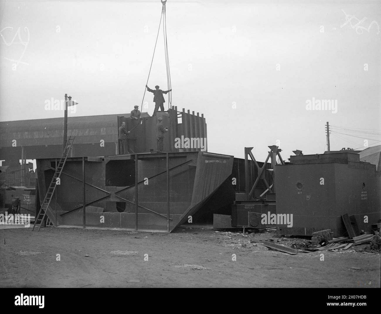 MEN AND WOMEN WHO BUILD BRITAIN'S FABRICATED SHIPS. APRIL 1944, THE BRITISH SHIPYARDS OF HENRY SCARR LTD, HESSLE NEAR HULL. - Men lifting off the crew's quarters from a pile of parts among which are a stern section and the engine room casing  Henry Scarr Ltd Stock Photo