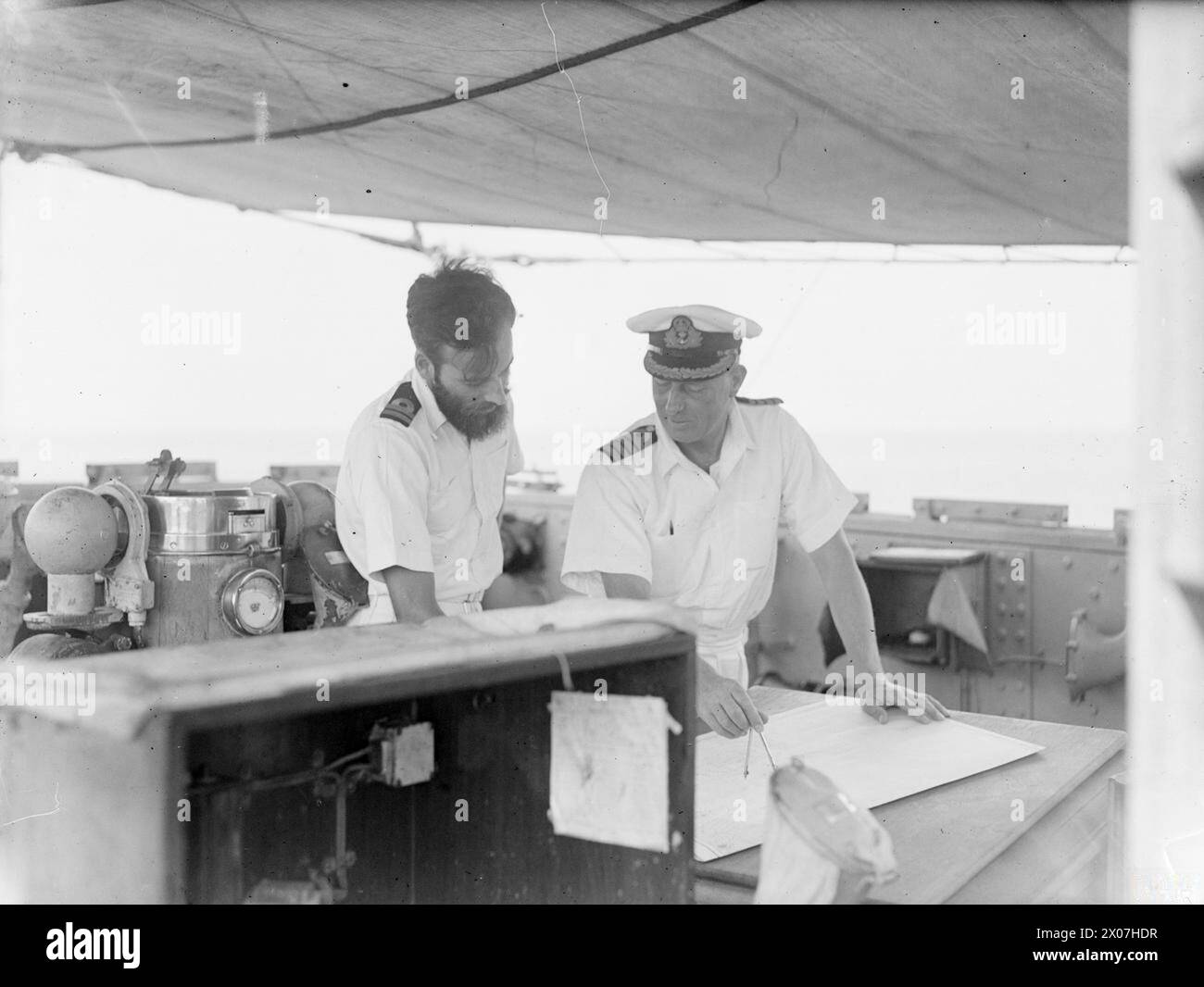 MAKING THE SEAS SAFE AGAIN. AUGUST 1945, AT SEA IN THE GULF OF GENOA. WITH THE 12TH MINESWEEPING FLOTILLA, OPERATING IN THE GULF OF GENOA UNDER THE COMMAND OF COMMANDER C SIMPSON, DSC, RN, COMMANDER MINESWEEPING WESTERN ITALY. THEY WORK FROM SURRENDERED ENEMY CHARTS AND ARE AIDED BY SUPERMARINE WALRUS AIRCRAFT AND THE US NAVY BLIMP MINE-SPOTTING DETACHMENT. - On the bridge of HM Minesweeper FLY Captain C W Rawlings, DSO and bar, DSC, RN, of Salisbury, Wilts, Senior Officer of the Flotilla, planning a sweeping operation with his navigator, Lieut A R B Sturdee, DSC, RN, of London Stock Photo