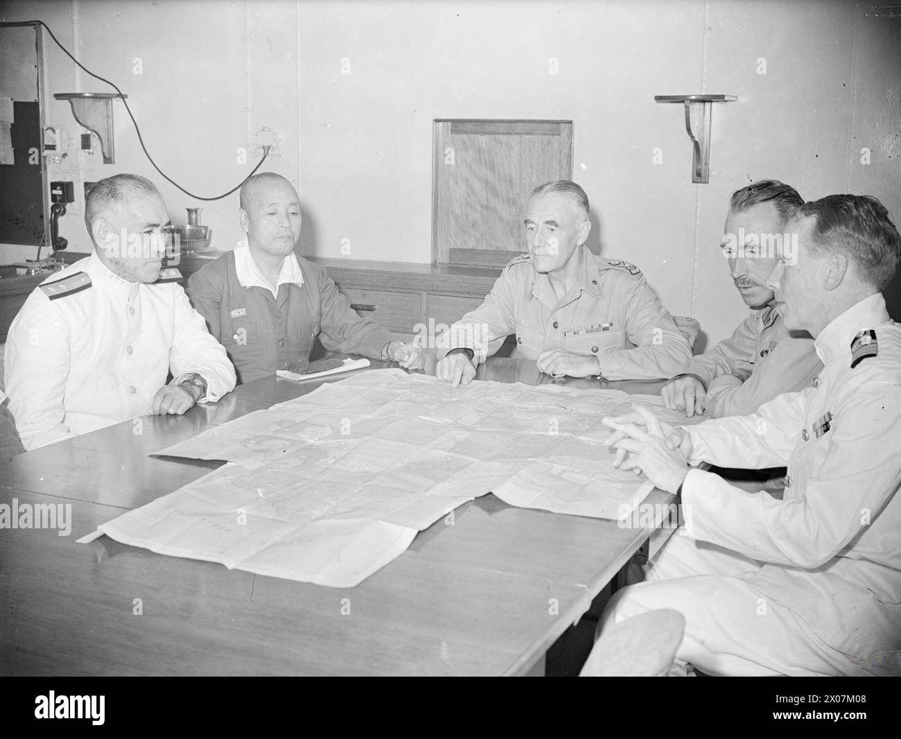 JAPANESE SOUTH-EASTERN ARMY CHIEF SURRENDERS ON BOARD HMS GLORY. 6 SEPTEMBER 1945, ON BOARD THE LIGHT FLEET CARRIER HMS GLORY, OFF RABAUL. THE SURRENDER OF THE JAPANESE IN THE SOUTH WEST PACIFIC AREA WAS SIGNED BY GENERAL IMAMURA, C IN C OF THE JAPANESE SOUTH EASTERN ARMY AND BY ADMIRAL JIN ICHA KUSAKA FOR THE JAPANESE SOUTH EASTERN NAVAL FORCES IN THAT AREA. - At the conference held in the captain's cabin. Left to right: Admiral Jin-Incha Kusaka, Commander Japanese S E Navy; General Imamura, General S E Japanese Army; Lieut General V A H Sturdee, GOC First Australian Army; Brigadier E L Sheeh Stock Photo