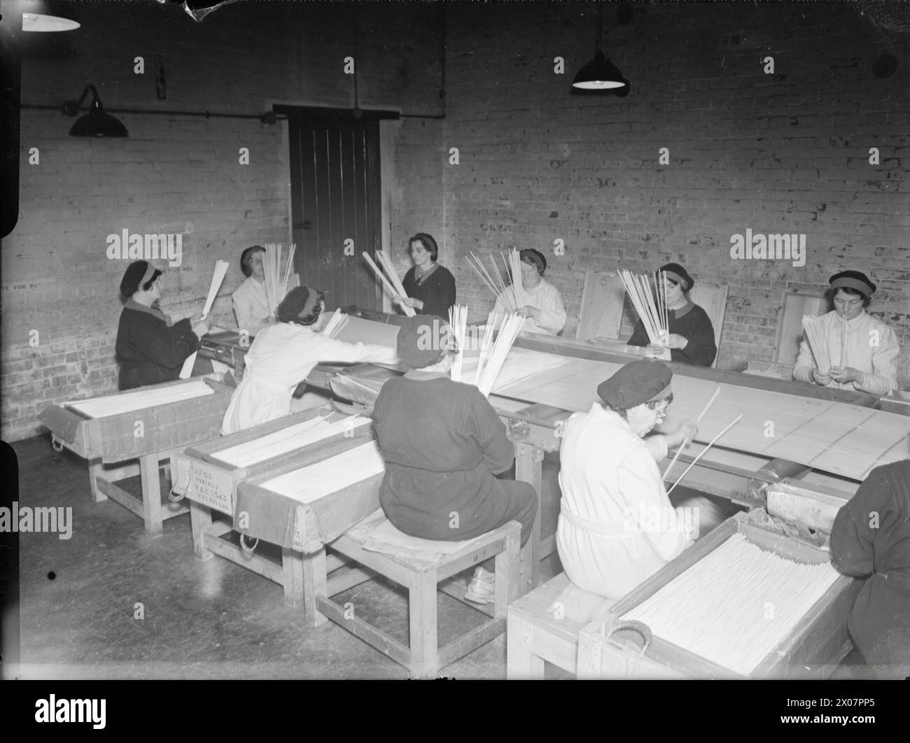 THE ROYAL NAVY DURING THE SECOND WORLD WAR - Female workers at an armament depot at a Royal Naval Cordite Factory, Holton Heath. They are armament factory clothing of coveralls and shoes and are seated around large tables. They are checking batches of cordite to ensure that each box is uniform in quality and size Stock Photo