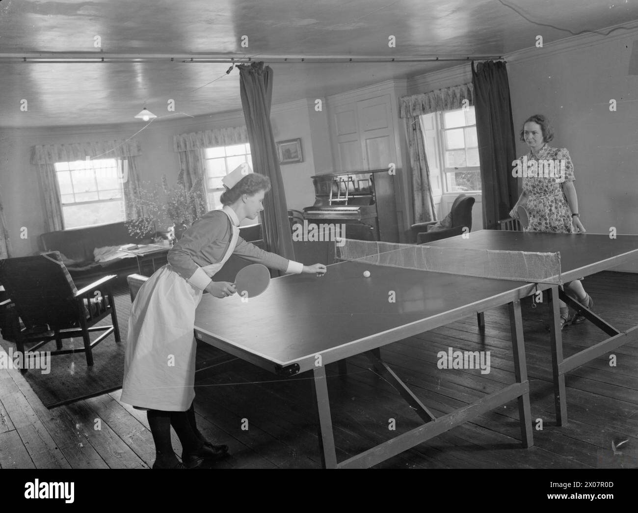 MANSION BECOMES MATERNITY HOME: LIFE AT BROCKET HALL, WELWYN, HERTFORDSHIRE, 1942 - Two nurses (one in uniform, the other in civilian clothes) play table tennis or 'ping-pong' in their sitting room after a busy day at Brocket Hall maternity hospital Stock Photo