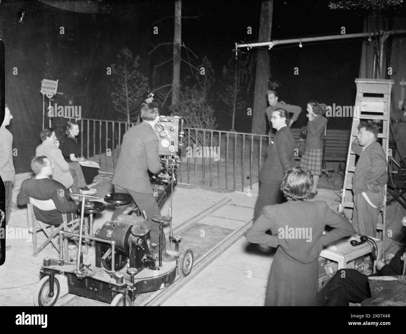 FOOTSTEPS IN THE NIGHT: THE PRODUCTION OF A MINISTRY OF INFORMATION FILM AT ELSTREE STUDIOS, ELSTREE, HERTFORDSHIRE, ENGLAND, UK, MAY 1941 - A scene on set taken during the production of a Ministry of Information film, released as 'Night Watch', starring Anne Firth as Sally and Cyril Chamberlain as Bill. The film was directed by Donald Taylor and made by the Strand Film Company for the Ministry of Information at Elstree Studios. Anne Firth and Cyril Chamberlain can be clearly seen beside a park bench in the right background. The camera and various members of the production team are clearly vis Stock Photo