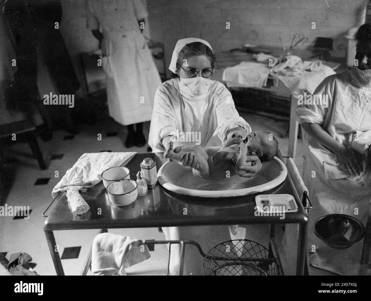 MANSION BECOMES MATERNITY HOME: LIFE AT BROCKET HALL, WELWYN, HERTFORDSHIRE, 1942 - A student nurse baths a baby at Brocket Hall. The nurse is wearing a surgical mask to prevent the spread of germs Stock Photo