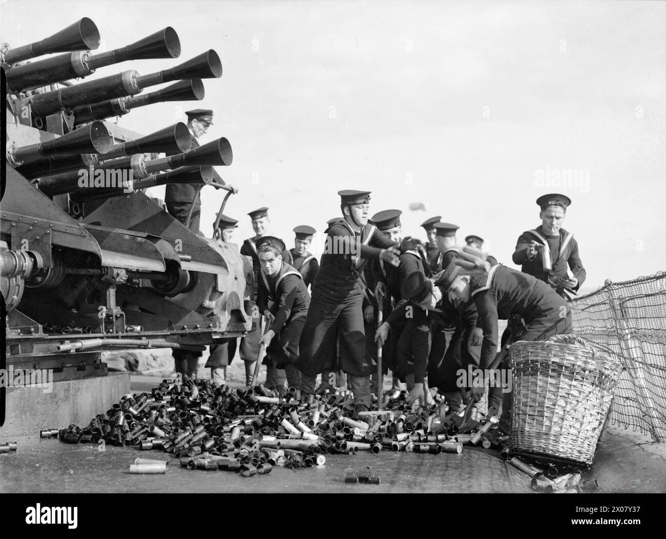 THE ROYAL NAVY DURING THE SECOND WORLD WAR - Naval ratings, under the watchful gaze of a NCO (left) sweep up spent cartridge cases for the eight barrelled, Vickers two pounder Mark VIII 'pom pom' gun. These ratings were firing live ammunition at the anti-aircraft gunnery school, Portsmouth Harbour Stock Photo