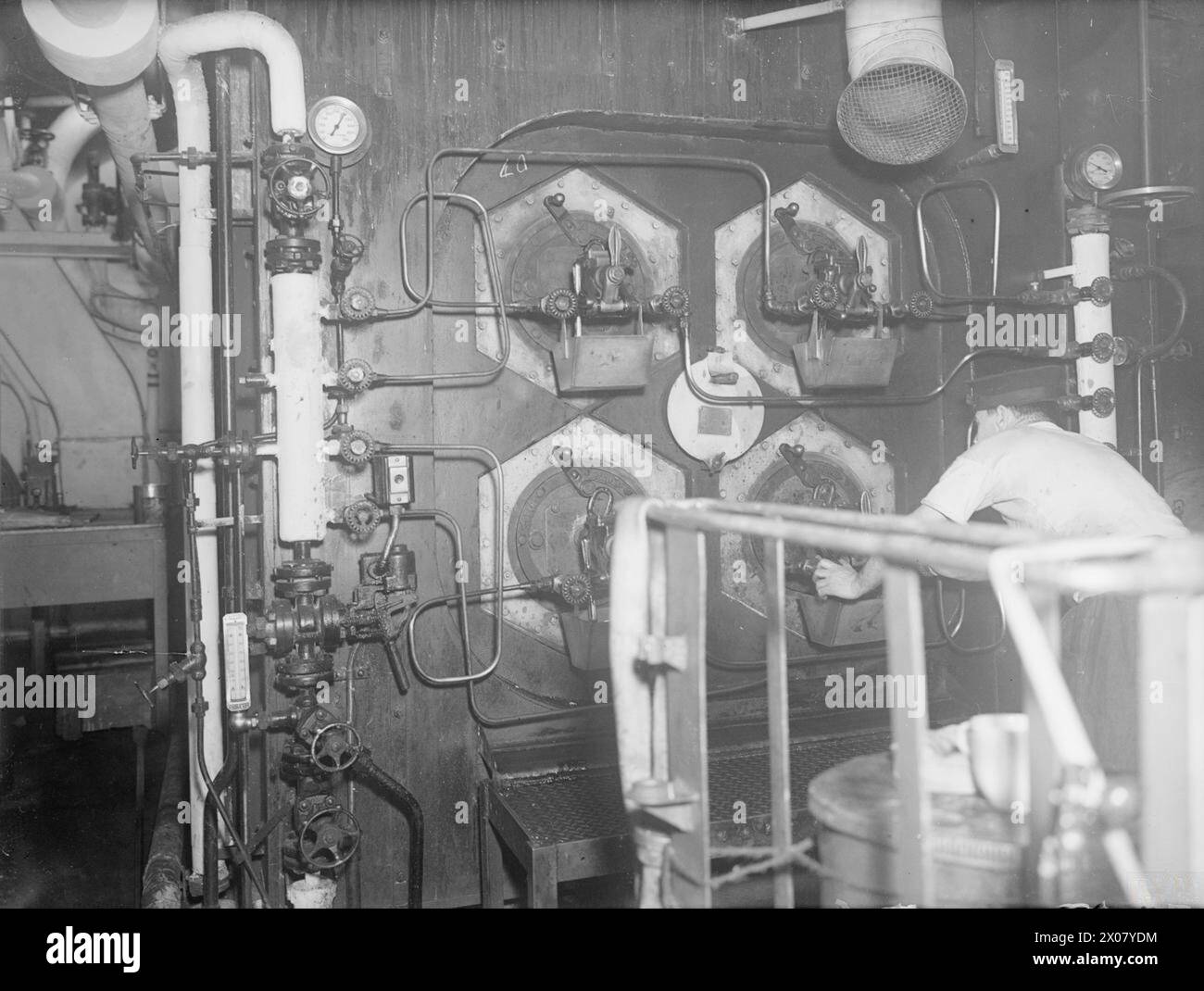 LIFE ON BOARD AN ESCORT CARRIER, HMS TRACKER. SEPTEMBER TO OCTOBER 1943, IN THE NORTH ATLANTIC. - A stoker adjusting one of the oil burners in the boiler room of HMS TRACKER Stock Photo