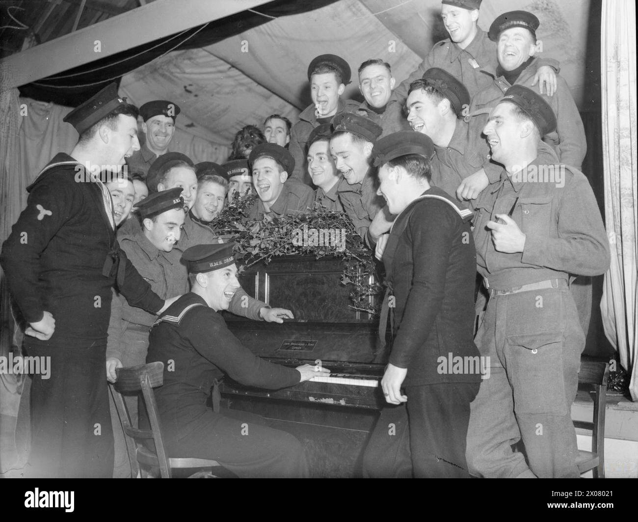 THE NAVY GETS READY FOR CHRISTMAS. DECEMBER 1940, HMS DRAKE, ROYAL NAVAL BARRACKS, DEVONPORT. BLUEJACKETS WHO WILL BE ON DUTY ON CHRISTMAS MAKING THE MOST OF IT, BY DECORATING THEIR MESS DECKS, ARRANGING CONCERTS, ETC. - Rehearsing for the concert at the Base. Sailors in battledress mount guard on Coast defence hence the mixture in uniforms Stock Photo