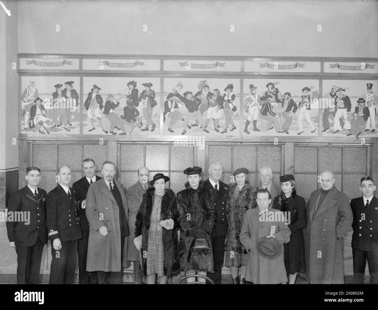 FAMOUS SCOTTISH ARTISTS VISIT A NAVAL CANTEEN. 21 JANUARY 1942, ROSYTH. SEVERAL WELL KNOWN ARTISTS VISITED A ROYAL NAVAL AND ROYAL MARINE CANTEEN, AND PAINTED THREE PANELS BY WAY OF A DECORATION. THE ARTISTS WERE MRS HASWELL MILLER, ARSA, ANNE REDPATH (NOW MRS MICHIE) AND MRS MARY ARMOUR, ARSA. MR W C HUTCHINSON ALSO VISITED THE CANTEEN TO SIGN HIS PAINTING OF THE BATTLE OF CAMPERDOWN. - The official party with Captain Benson centre, in front of one of the three panels Stock Photo