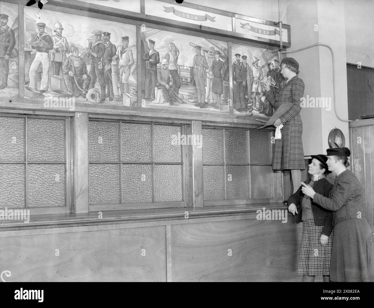 FAMOUS SCOTTISH ARTISTS VISIT A NAVAL CANTEEN. 21 JANUARY 1942, ROSYTH. SEVERAL WELL KNOWN ARTISTS VISITED A ROYAL NAVAL AND ROYAL MARINE CANTEEN, AND PAINTED THREE PANELS BY WAY OF A DECORATION. THE ARTISTS WERE MRS HASWELL MILLER, ARSA, ANNE REDPATH (NOW MRS MICHIE) AND MRS MARY ARMOUR, ARSA. MR W C HUTCHINSON ALSO VISITED THE CANTEEN TO SIGN HIS PAINTING OF THE BATTLE OF CAMPERDOWN. - Mrs Haswell Miller adding some finishing touches to her panel while Mrs Mary Armour and Anne Redpath look on Stock Photo