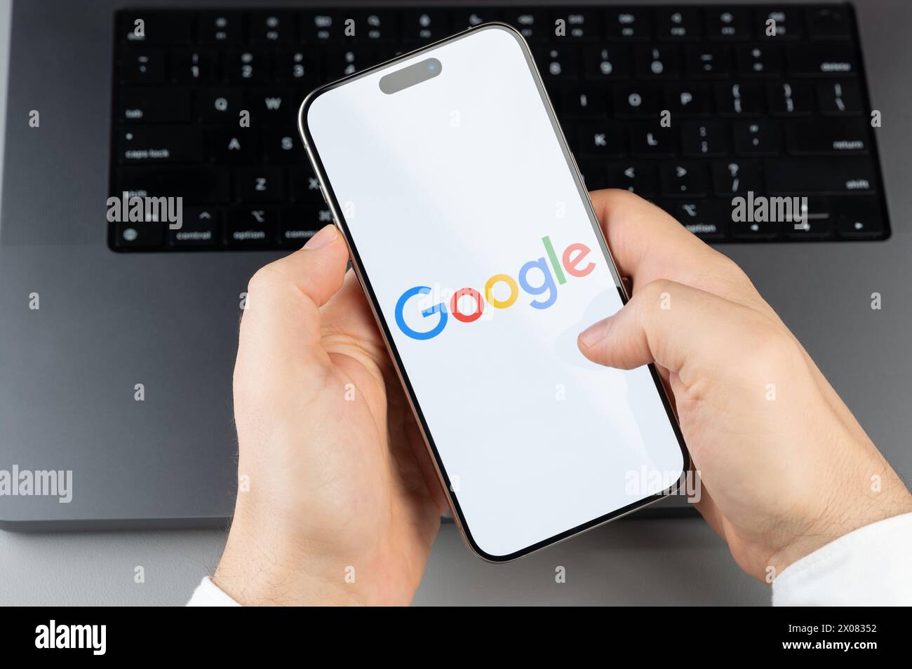 New York, USA - April 6, 2024: Popular Google mobile app on smartphone screen in hands on laptop keyboard background Stock Photo