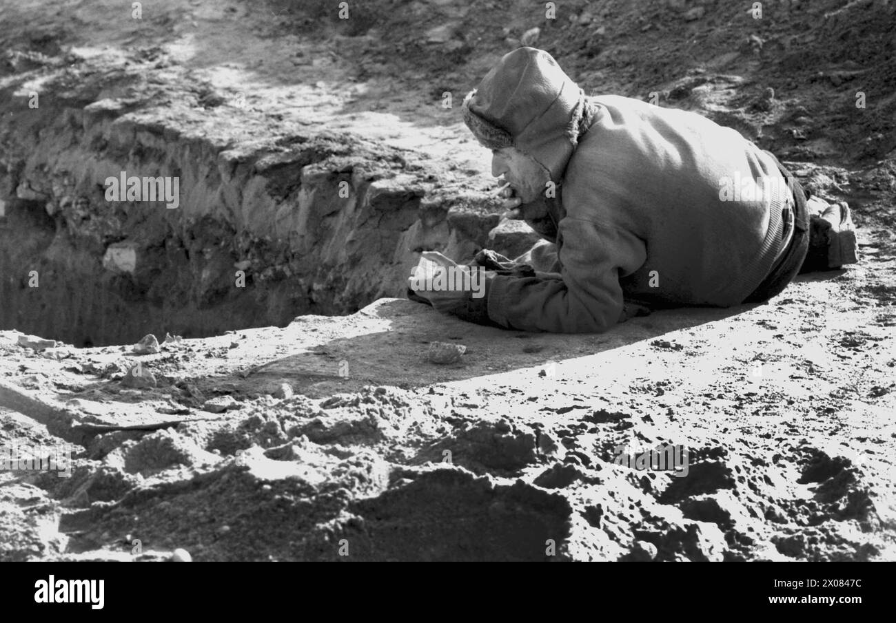 Socialist Republic of Romania, approx. 1980. Homeless man laying on the ground, smoking a cigarette at the edge of a trench. Stock Photo