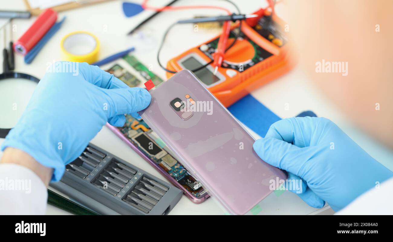 Technician repairs broken smartphone at table in workshop Stock Photo