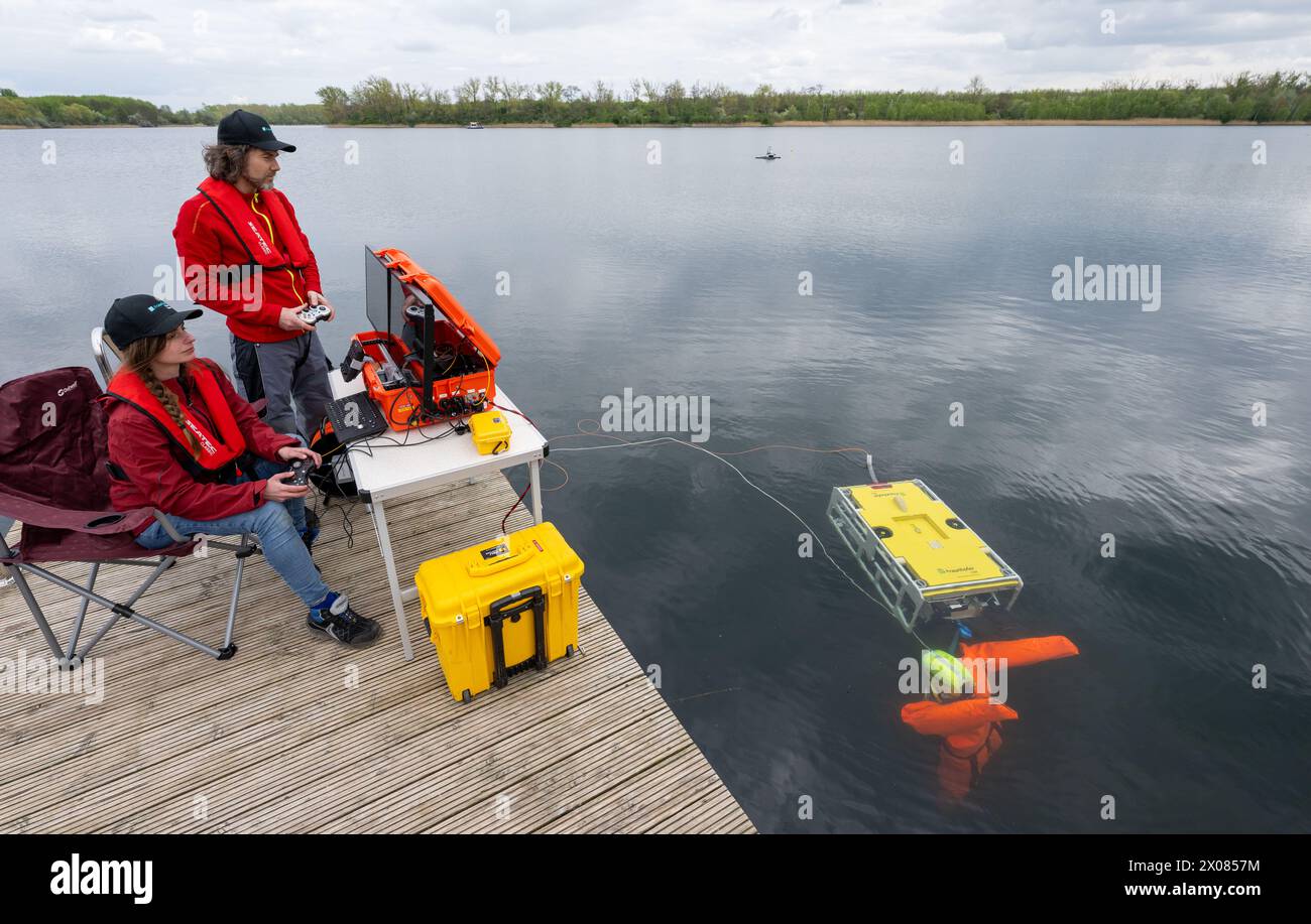 10 April 2024, Saxony-Anhalt, Halle (Saale): Regina Thomas and Sebastian Matz from the Fraunhofer Institute IOSB-AST in Ilmenau demonstrate the use of a diving robot at Hufeiesensee in Halle/Saale. The DRK water rescue service in Halle is testing the use of robotic systems supported by artificial intelligence (AI) that can help with rescues at Hufeisensee. According to the water rescue service, this is the first test of its kind in Germany. The system is able to scan large areas of water in search of people and objects in just a few minutes. A DRK water rescue education and training center wil Stock Photo