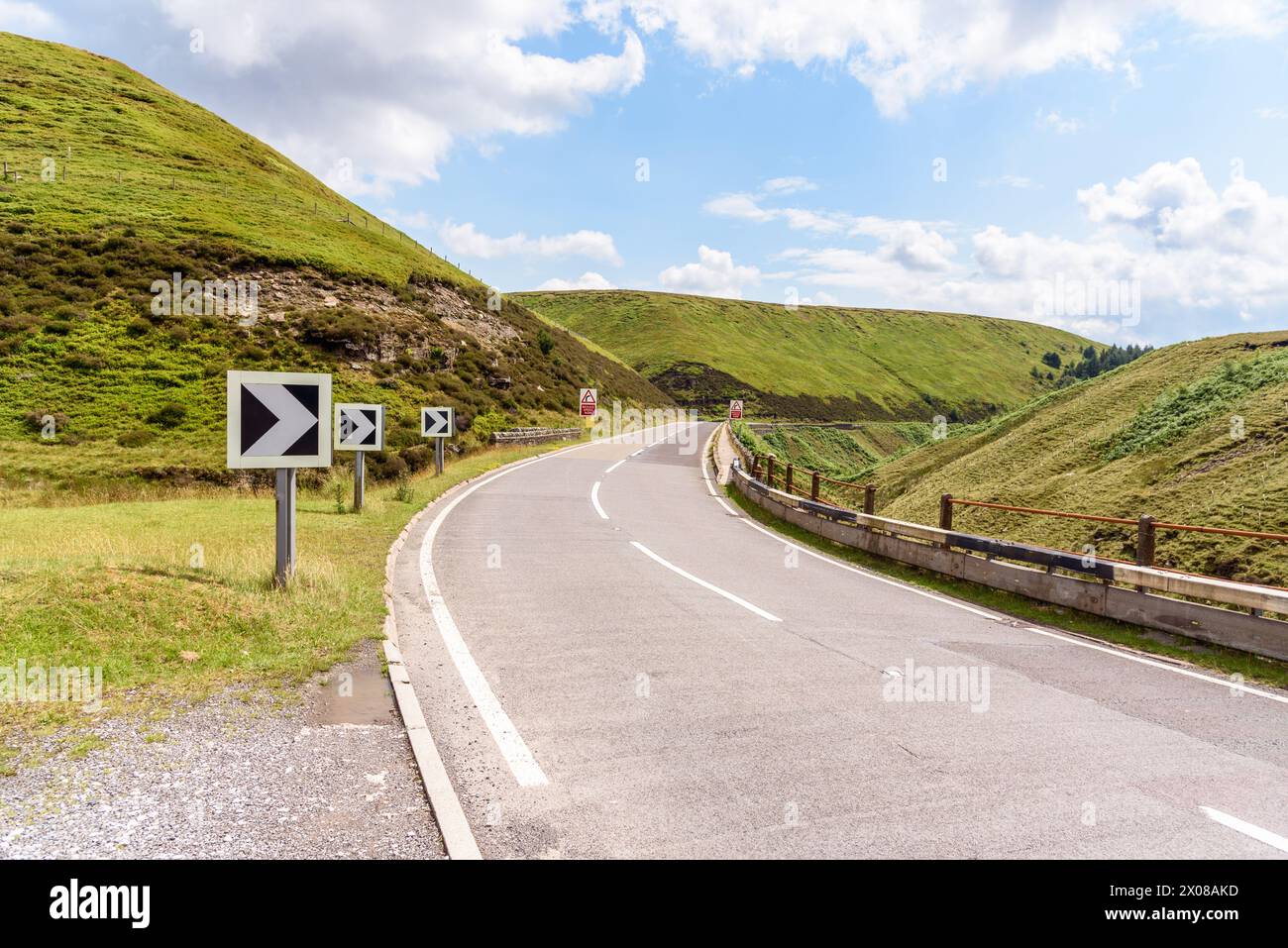 Chevron road signs along a sharp bend along a winding mountain pass road in England on a partly cloudy summer day Stock Photo