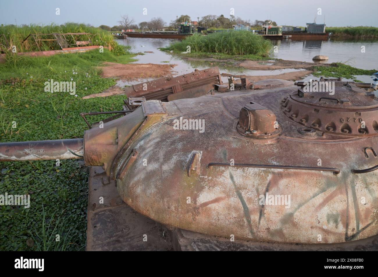 SOUTH SUDAN, Upper Nile state, town Renk, river White Nile, abandoned wreck of soviet russian made battle tank T-54 of SPLA Sudan Peoples Liberation Army from the second sudanese civil war with North Sudan SAF Sudan Armed Forces, behind river barge for transport of goods and passenger to Malakal Stock Photo